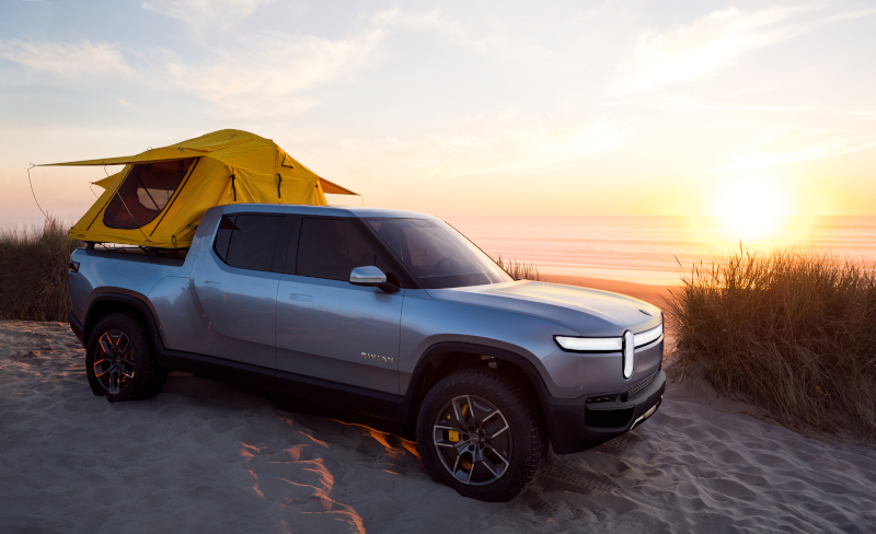 Beachside Camping with Electric Pickup Truck An electric pickup truck with a rooftop tent parked on a sandy beach at sunset, with the ocean horizon in the background.